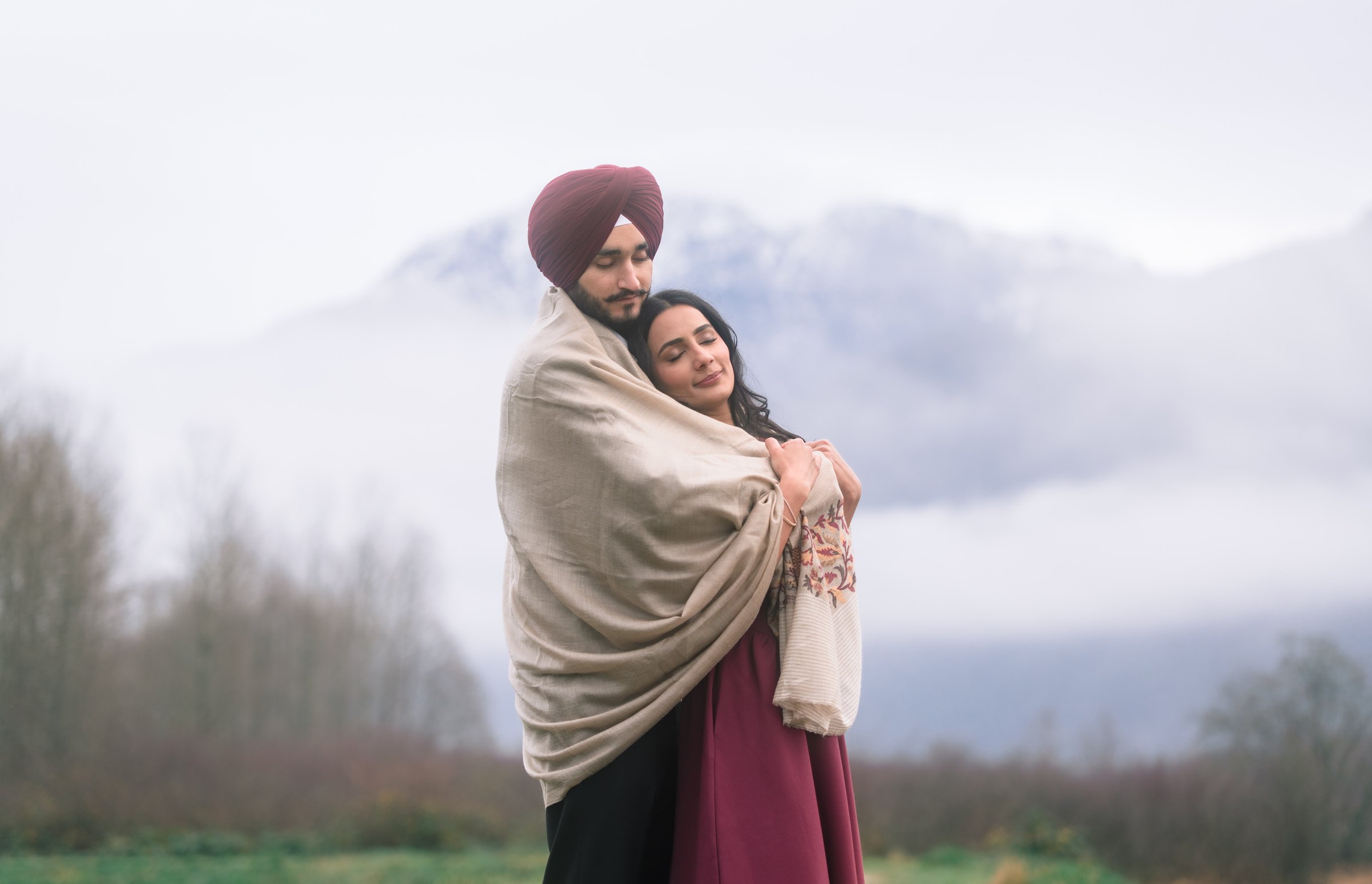 Intimate couple portrait of Simar & Manjeet embracing in the low mountain clouds at Pitt Lake in Pitt Meadows, BC — White Daisy Weddings